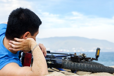 Men with his bicycle lying on a beach.の写真素材