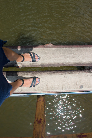 The tourists woman legs are crossing dry streams with a bridge made of bamboo trunks. In the path of natureの写真素材