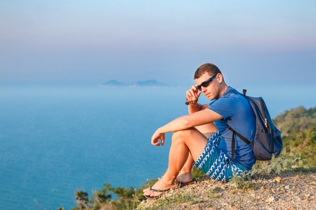 man in sunglasses sits on the edge of a mountain.の写真素材