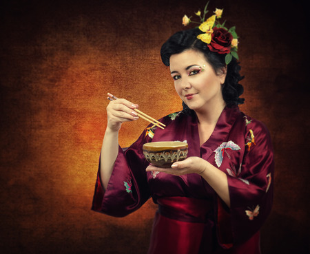 Flowers haired kimono caucasian woman eating someting from a bowl with chopsticks on grunge backgroundの写真素材