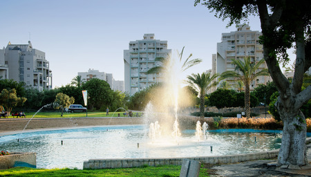 Small pond with fountain at sunset on apartment buildings background in green city park. Ha-Zikaron Garden, Rishon Le Zion, Israelのeditorial素材