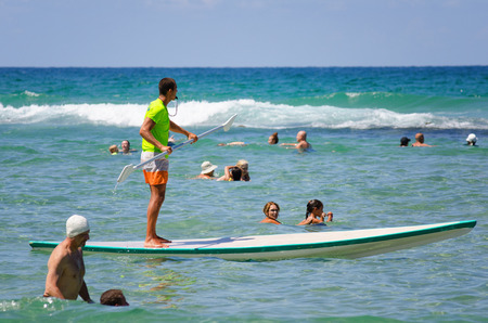 Bat Yam, Israel - September 6, 2014: Bat Yam beach patrol. Beach lifeguard stand up paddling on the Mediterranean sea in Bat Yam city, Israel. People swim near a lifeguardのeditorial素材