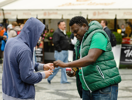 Prague, Czech Republic - September 26, 2014:  In Old Town, white young man in hooded jacket gives a cigarette to black guy dressed in sleeveless pufferのeditorial素材