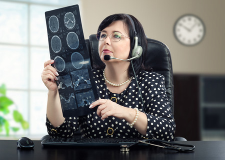 Telemedicine doctor in headphones is looking at x ray picture of brain carefully