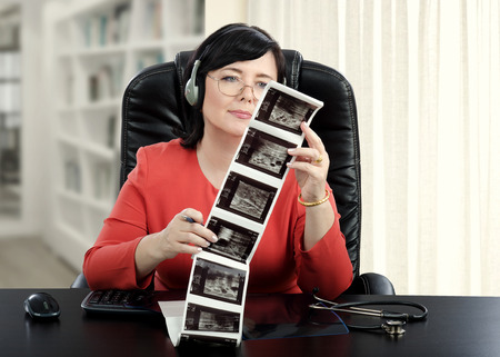 Female online doctor in headset sitting at the desk exams at ultrasound mammogram results attentivelyの写真素材