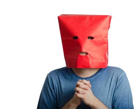 Introverted young man with clenched hands wears red paper bag over head because he is lacking in confidenceの写真素材