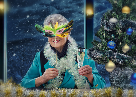 Senior woman in feather mask toasting a Merry Christmas and a Happy New Year with glass of sparkling wineの写真素材