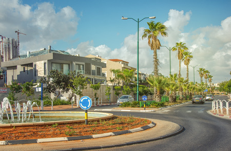 Rishon LeZion, Israel-May 27, 2016:Traffic circle with small fountain on Heil HaTothanim Street. Tree private cars riding on the street with green palms. 2-story houses are seen in left siteのeditorial素材