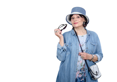 Elegant senior woman in denim clothes posing on white background. She wears striped denim bucket...