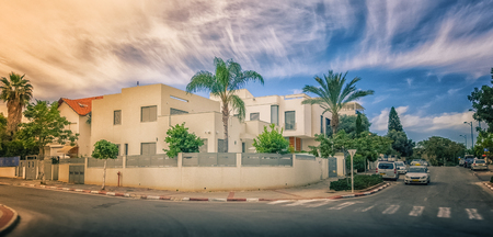 Rishon LeZion, Israel-February 18, 2016: View of modern two-story house under beautiful sky. The home is surrounded semi-circular fence, green trees and palms. Urban asphalt road in a foreground. Bright sunny day. It is located at intersection Graetz and のeditorial素材