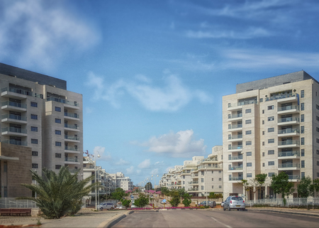 Nes Ziona, Israel-March 20, 2016: Front view of two white gray new 8 story residential buildings are located on both sides of the beginning of Khoshen street. Wide road and blue sky. Horizontal shotのeditorial素材