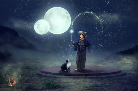 Older fairy with magic wand and black cat performs a magical ritual with two moonsの写真素材