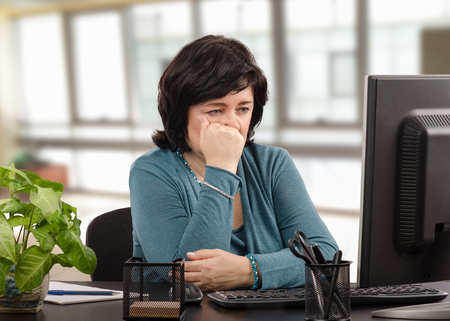Sad middle-aged business woman weeps looking at computer monitor because her business is in bankruptcyの写真素材