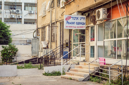 Rishon LeTsiyon, Israel-June 23, 2017: The Russian and Hebrew signboard over the shop says that it is a tailoring repairs shop. The 5 steps staircase with a white railing leads to the shop. The house basement on the right and entrance to the apartment buiのeditorial素材