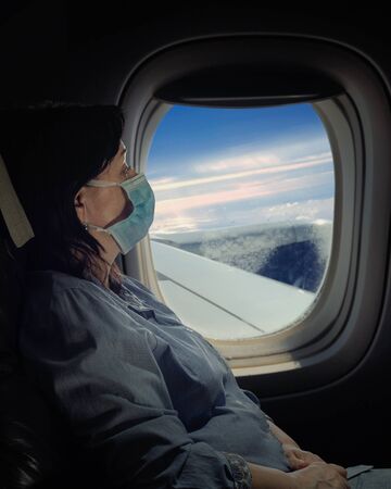 Mature woman in face mask traveling on the airplane. Night shot opposite plane window.の写真素材