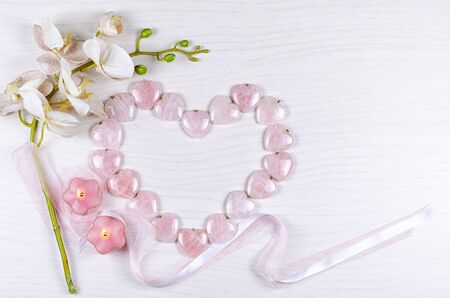 Big rose quartz heart compilated from same pendants, an artificial textile sprig of orchid, two candles lit and silk ribbons create the flat lay composition. Top view, copy space.の写真素材