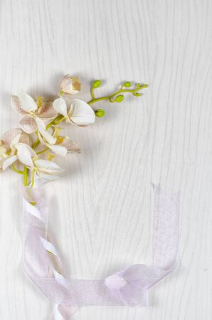 An artificial textile sprig of orchid with the green stem wrapped by two silk ribbons lays on a light gray wooden background. Top view, copy space.の写真素材