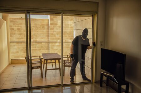 Thief in black balaclava comes inside the home because the homeowner forgot to close the sliding...