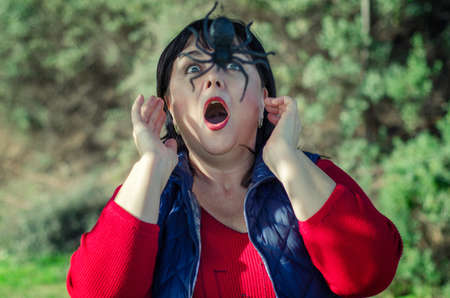 Mature woman in a red shirt and blue overcoat hikes in the garden and runs into a huge black spider.の写真素材