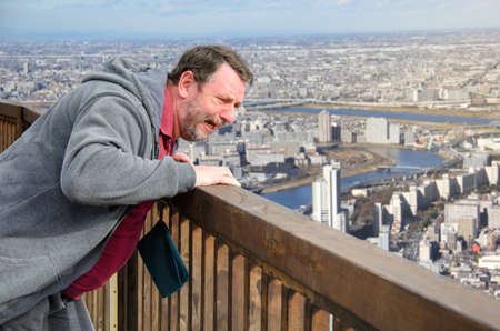 A mature man is afraid of heights. He stands on the observation deck and looks down at the panoramic...