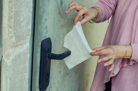A woman experiences obsessive thoughts about germs and takes a hygiene napkin to cover the door handle of the entrance door. She suffers from mysophobia.の写真素材