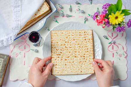 Hands had just pulled the matzo out of the pack and put it on a white plate. The table is covered...