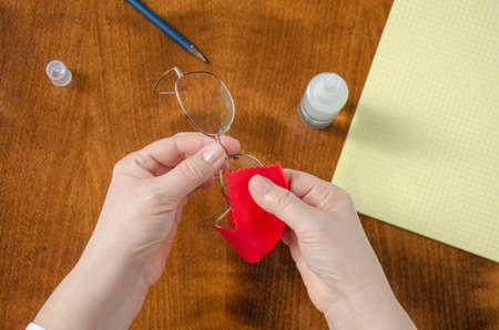 Woman rubs gentle glasses with a red cloth on the background of the wooden desk in the office. Top view.の写真素材