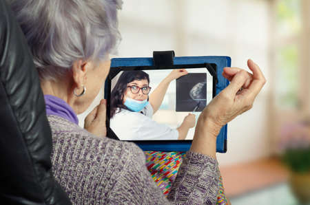 Telemedicine doctor in white uniform and blue face protective mask explains to a geriatric patient...