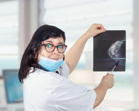 Doctor in white uniform and blue mask shows x-ray image of female breastの写真素材