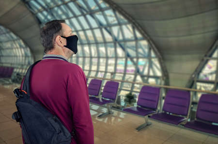 Mature man in a black face mask scrutinizes the interior design of an unfilled airport.の写真素材