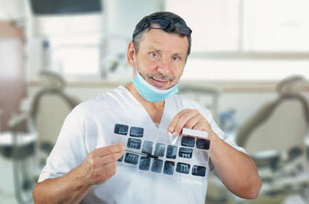 Amiable male dentist in white uniform explains something while holding dental x-rays imagesの写真素材