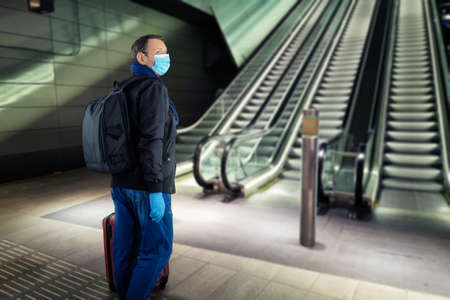Mature traveler in a protective mask and gloves looks around near the subway escalator on an empty platform.の写真素材
