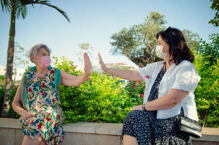 Carer and senior adult woman demonstrate air five gesture. Their palms do not touch. Their faces in protective masks as required during the pandemicの写真素材