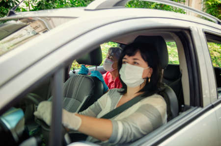 Carer drives a senior adult woman to planned outings or events. Both wear protective masks. The face of the caregiver is slightly blurred, the old lady is in focus.の写真素材