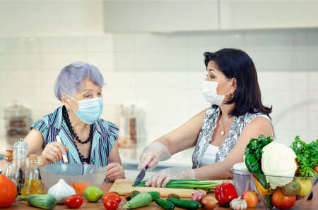 A kind volunteer continues to visit a lonely old woman to help her in the kitchen. Even during a pandemic. Only both women wearing protective masks.の写真素材