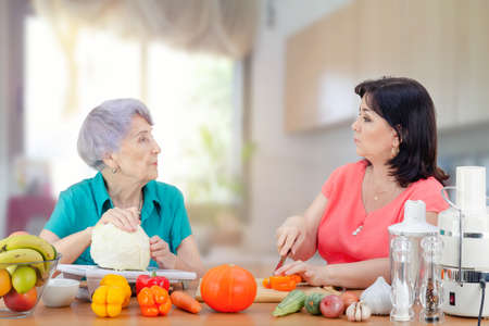 A kindly daughter or hired actress from a rental family service regularly visits her old mother or customer to cook a vegetable dish together. It is very important to pay attention to elderly parents.の写真素材