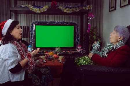 A caregiver and an elderly woman singing in front of a chroma key TV screen on Christmas Eve. The room is decorated with tinsels.の写真素材