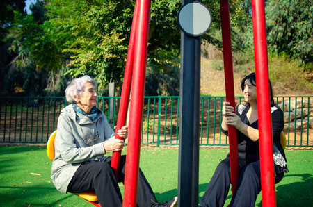 Two elderly women are working out in an outdoor fitness field with pleasure. Someone younger can be a caretaker or a volunteer or just a loving daughter.の写真素材