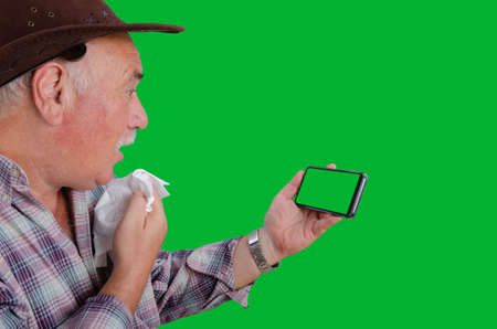 Senior Farmerâs Open-Mouth Reaction to Smartphone Screen, Napkin in Hand, Captured Against Green Chroma Key Backgroundの写真素材
