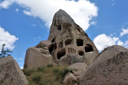 The amazing cliffs of Cappadocia, where people lived in caves for a long time. Against the background of a blue sky with white clouds, a rock with windows cut into it. Mysteriously.の写真素材
