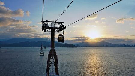Sunset. Cableway across the bay in Vietnam. The sun is hiding behind clouds, on calm water a sun...