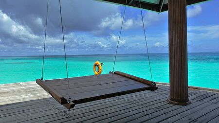 A delightful vacation in the middle of the ocean. A swing is suspended on a wooden platform in the...