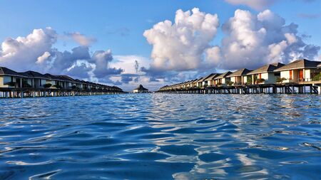 Maldives picture. Above the surface of the turquoise ocean are two rows of villas. The ocean is calm...