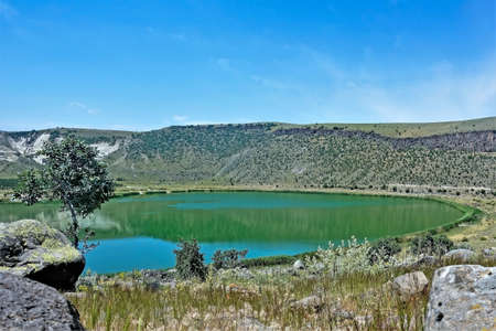 Lake Nar in the crater of an extinct volcano. A round reservoir of emerald water is surrounded by...
