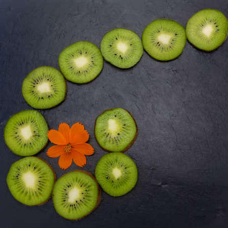 Kiwi fruits were cut into circles and laid out on a black stone tile. Composition in the form of a...