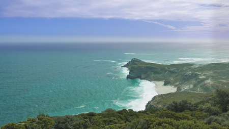 The legendary rocky Cape of Good Hope juts out into the ocean. A small sandy beach is visible, waves...