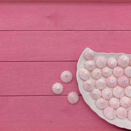 On a bright pink plank surface, there is a white platter with small delicate pink meringues. Three cakes are next to each other. View from above.の写真素材