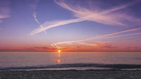 Sunset over the sea. The sun is low on the horizon. The sky is highlighted in orange, you can see...