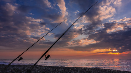 Sea fishing at sunset. Two fishing rods stand obliquely on a pebble beach. The clouds in the blue...