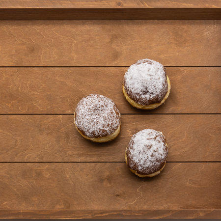 Three fresh donuts topped with powdered sugar. The pastries are on a beige wooden plank tray. Top view.の写真素材